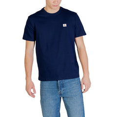 Image 1 : T-shirt Calvin Klein Jeans homme bleu marine avec badge logo CK cousu sur la poitrine gauche, porté avec un jean clair — Delvale